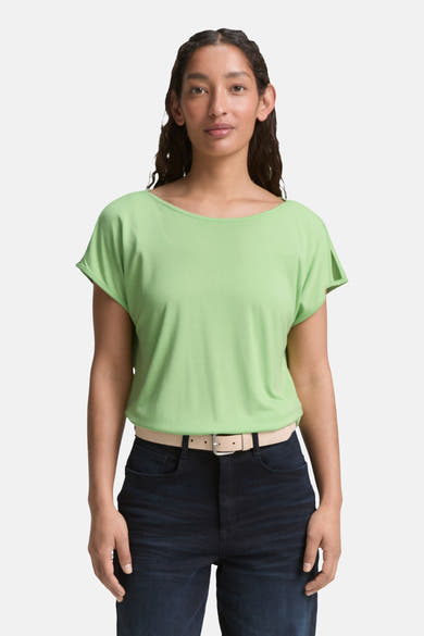 Blouse verte à manches courtes par Tom Tailor, avec ceinture claire et pantalon foncé.
