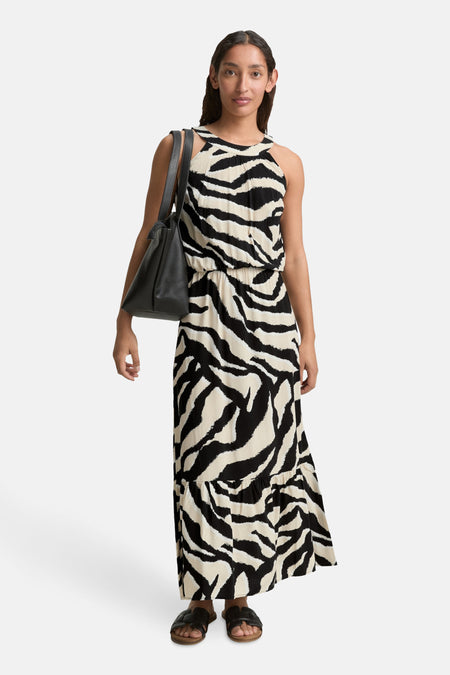 Multikleurige lange jurk van Tom Tailor met zebraprint, gedragen met een zwarte handtas en platte sandalen.