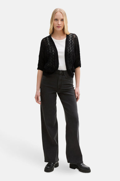 Zwarte, opengewerkte gebreide gilet van Tom Tailor, gedragen over een eenvoudig wit T-shirt en een zwarte high-waist jeans.