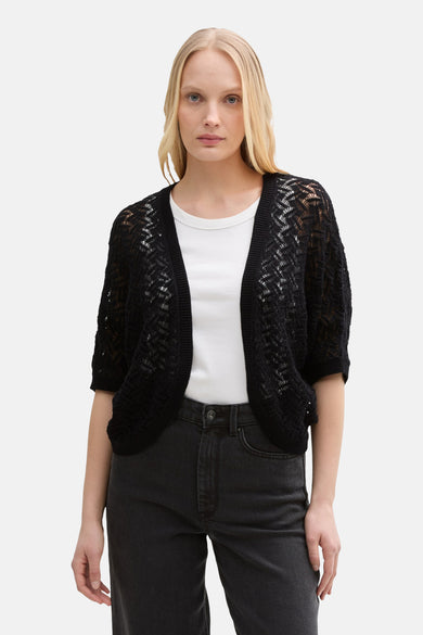 Zwarte, opengewerkte gebreide gilet van Tom Tailor, gedragen over een wit T-shirt en een zwarte jeans.