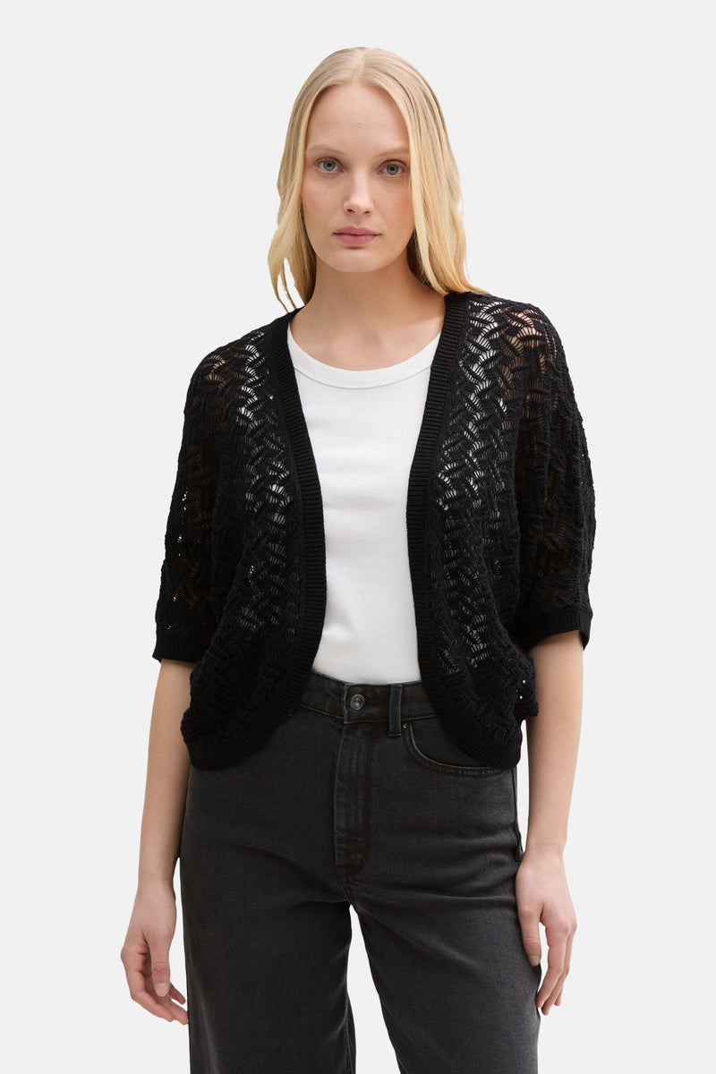 Zwarte, opengewerkte gebreide gilet van Tom Tailor, gedragen over een wit T-shirt en een zwarte jeans.