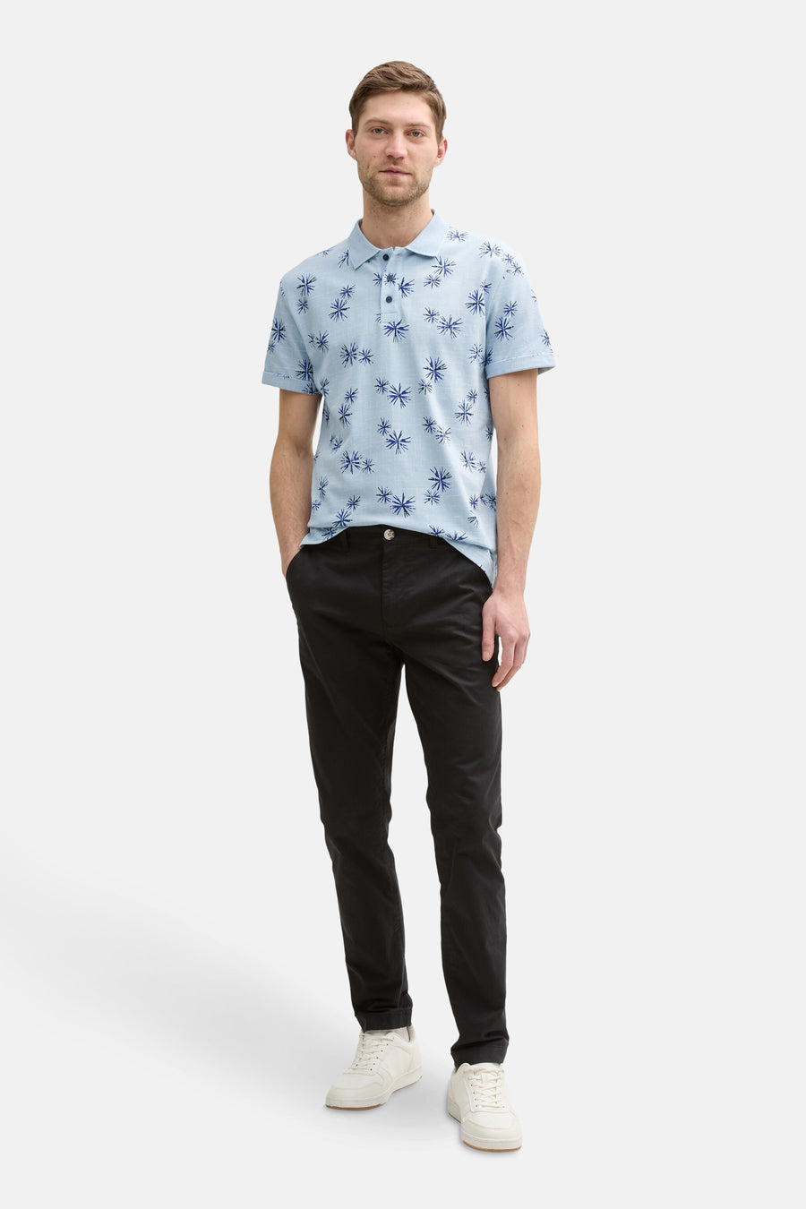 Blauw poloshirt met korte mouwen van Tom Tailor, met blauw bloemenpatroon, gedragen met een zwarte broek en witte sneakers.