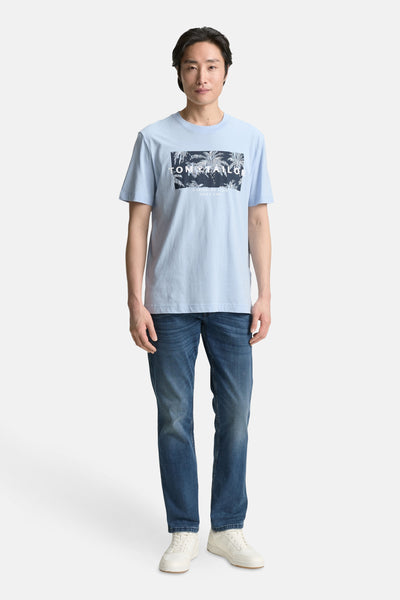 Blauw T-shirt met korte mouwen van Tom Tailor, met grafische print voor, gedragen met een spijkerbroek en witte sneakers.