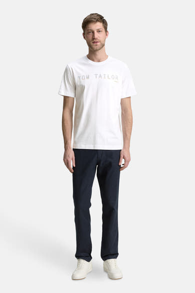 T-shirt blanc à manches courtes de Tom Tailor, porté avec un pantalon bleu marine et des baskets blanches.
