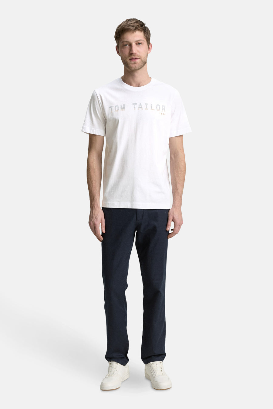T-shirt blanc à manches courtes de Tom Tailor, porté avec un pantalon bleu marine et des baskets blanches.
