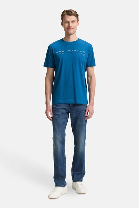 Blauw T-shirt met korte mouwen van Tom Tailor, gedragen met een spijkerbroek en witte sneakers.