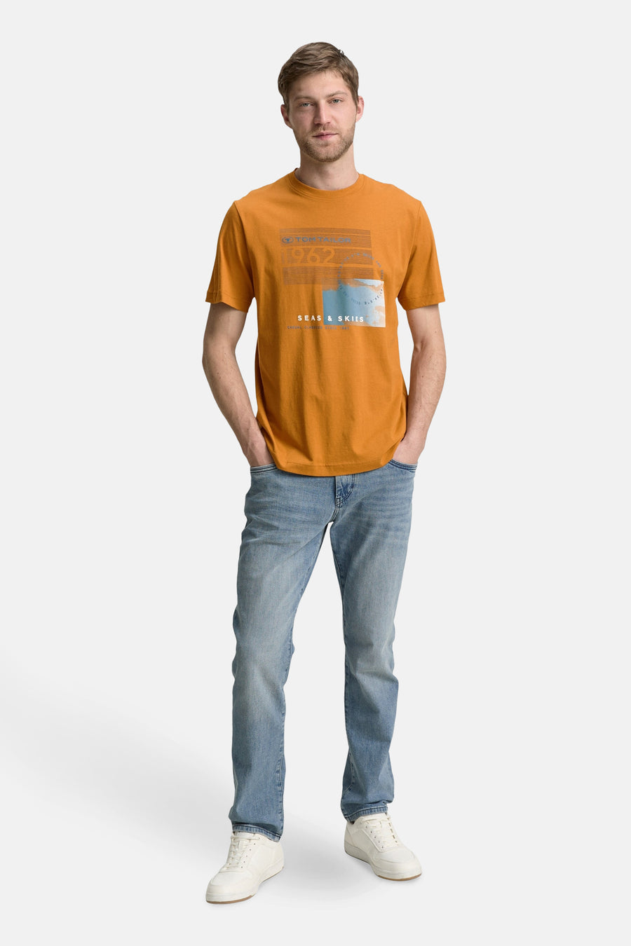 T-shirt ocre à manches courtes de Tom Tailor, avec imprimé graphique sur le devant, porté avec un jean et des baskets blanches.
