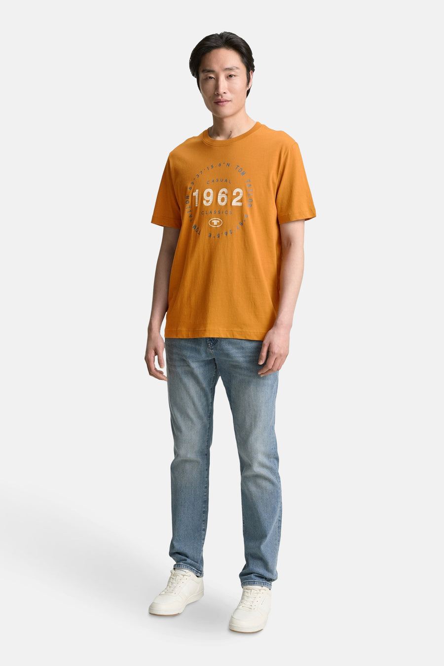 T-shirt ocre à manches courtes de Tom Tailor, avec motif imprimé sur le devant, porté avec un jean et des baskets blanches.