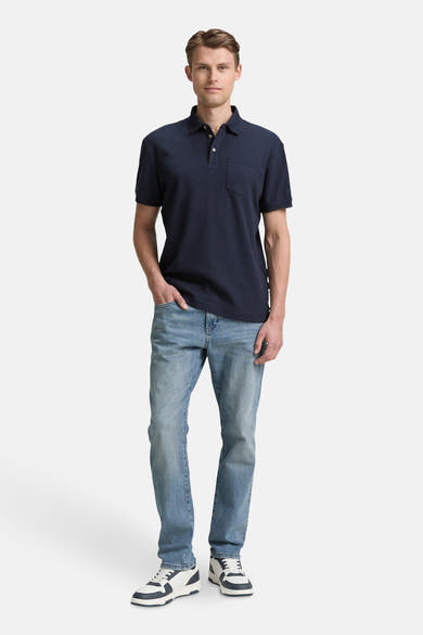 Blauw poloshirt met korte mouwen van Tom Tailor, gedragen met een verbleekte spijkerbroek en tweekleurige sneakers.