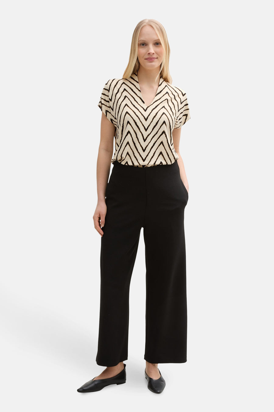 Chemisier multicolore à manches courtes de Tom Tailor, avec un motif à chevrons noir et beige, porté avec un pantalon noir large et des ballerines noires.