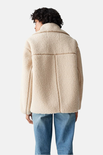 Veste courte beige de OPUS, en peau lainée avec col à revers, portée avec un jean bleu.