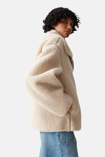 Veste courte beige d'OPUS en imitation peau de mouton avec poches et portée sur un jean bleu.