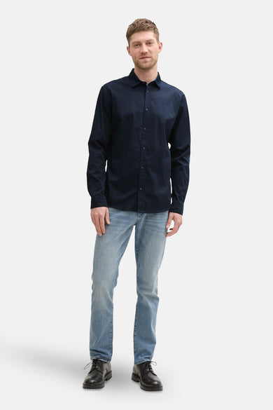 Chemise à manches longues bleu foncé de Tom Tailor, portée avec un jean clair et des chaussures en cuir noir.
