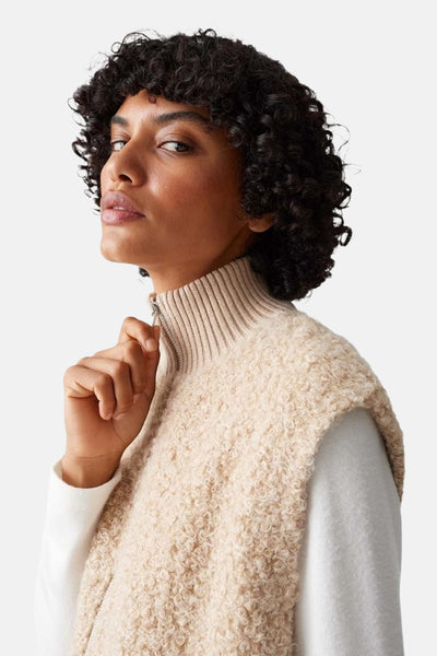 Pull écru à col rond par OPUS, porté avec un gilet texturé couleur crème et un col zippé.