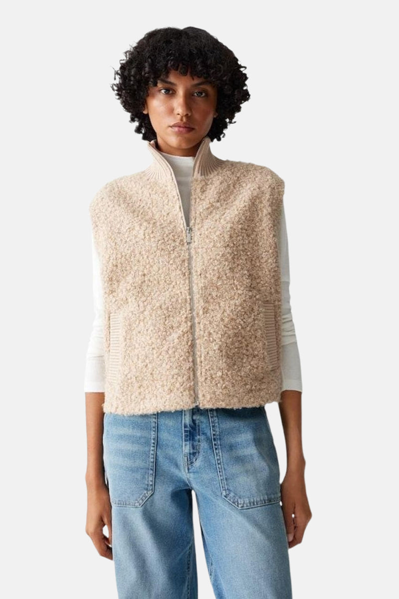 Gilet sans manches beige effet mouton, par OPUS, porté sur un pull col roulé blanc et un jean taille haute bleu.