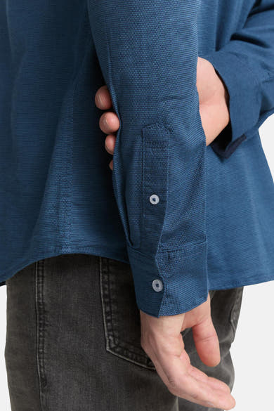 Blauw overhemd met lange mouwen van Tom Tailor, knoopdetail bij de manchet, op een donkergrijze jeans.