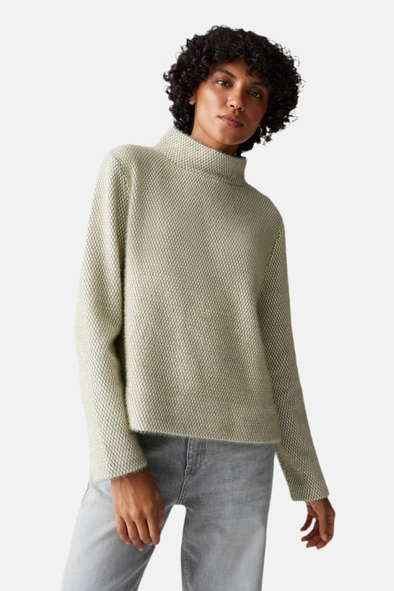 Pull vert texturé par OPUS, porté avec un jean gris clair.
