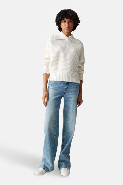 Pull beige en maille texturée par OPUS, porté avec un jean bleu ample et des chaussures blanches.
