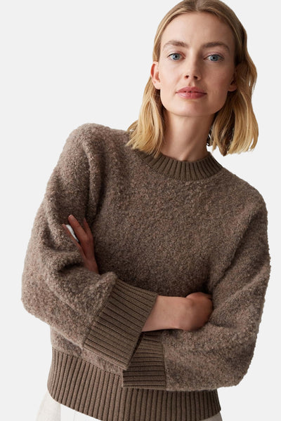Pull à col rond brun d'OPUS, en maille texturée, porté par une femme aux bras croisés.