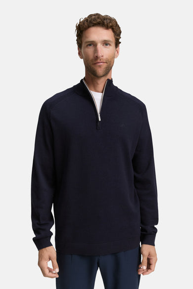 Blauwe trui met ronde hals van Tom Tailor, gedragen met een marineblauwe plooibroek en witte sneakers.