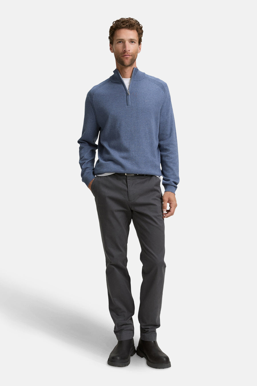 Blauwe trui met ronde hals van Tom Tailor, gedragen met een grijze broek en zwarte enkellaarsjes.