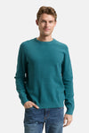Pull à col rond vert par Tom Tailor porté avec un jean décontracté, l'homme a une main dans la poche.