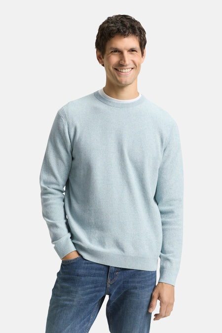 Pull à col rond bleu by Tom Tailor, porté avec un jean et un t-shirt blanc, sur fond uni.