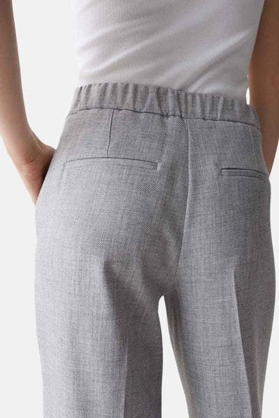 Pantalon de costume gris by OPUS, avec ceinture élastique et poches arrière passepoilées, porté avec un haut blanc.
