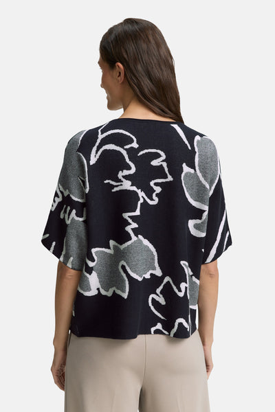 Ronde hals blauwe trui van Tom Tailor, met grijs-witte bloemenprint, gedragen met een beige broek.