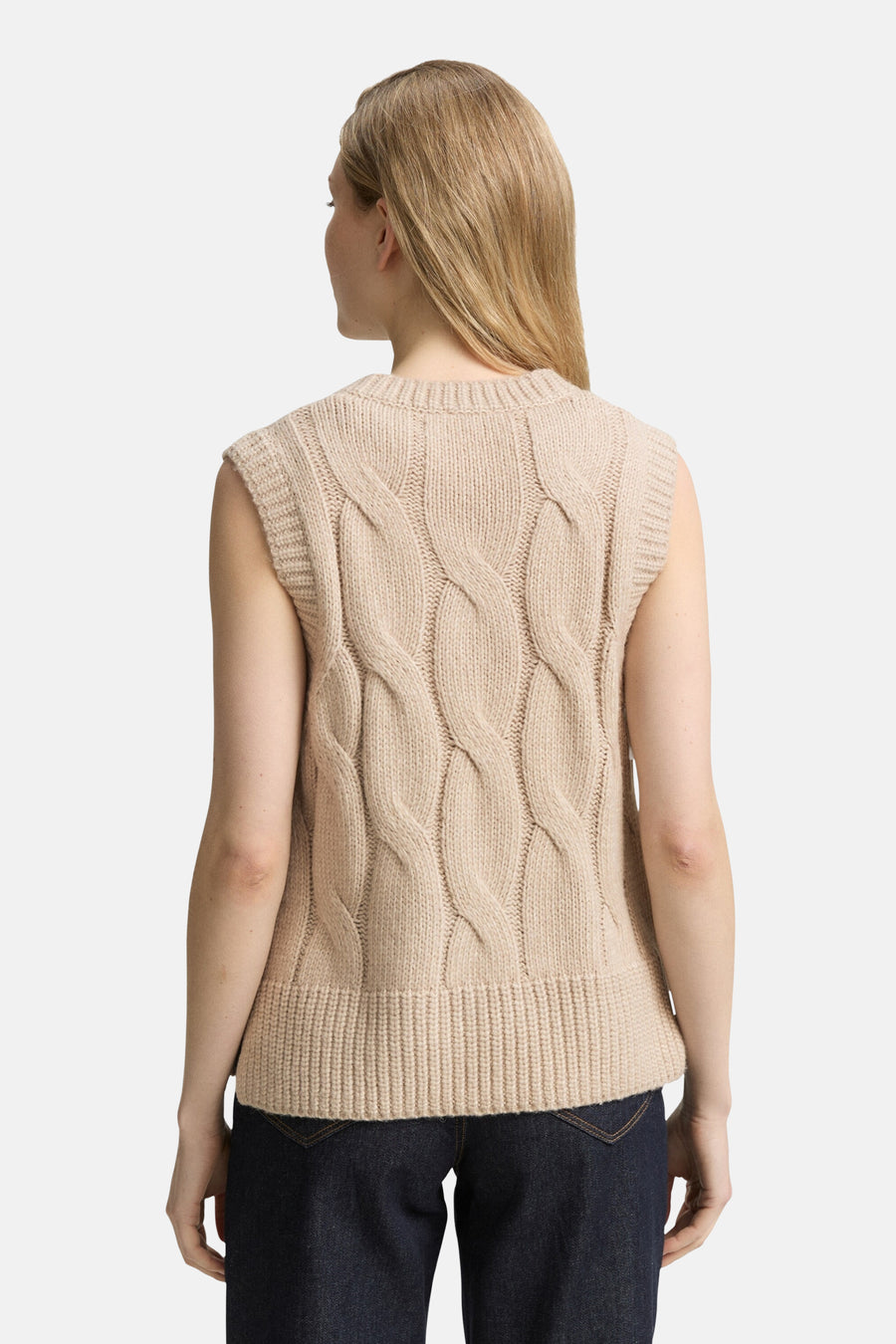 Beige gebreid hemdje van Tom Tailor, met kabelpatronen op de rug, gedragen over een donkerblauwe jeans.