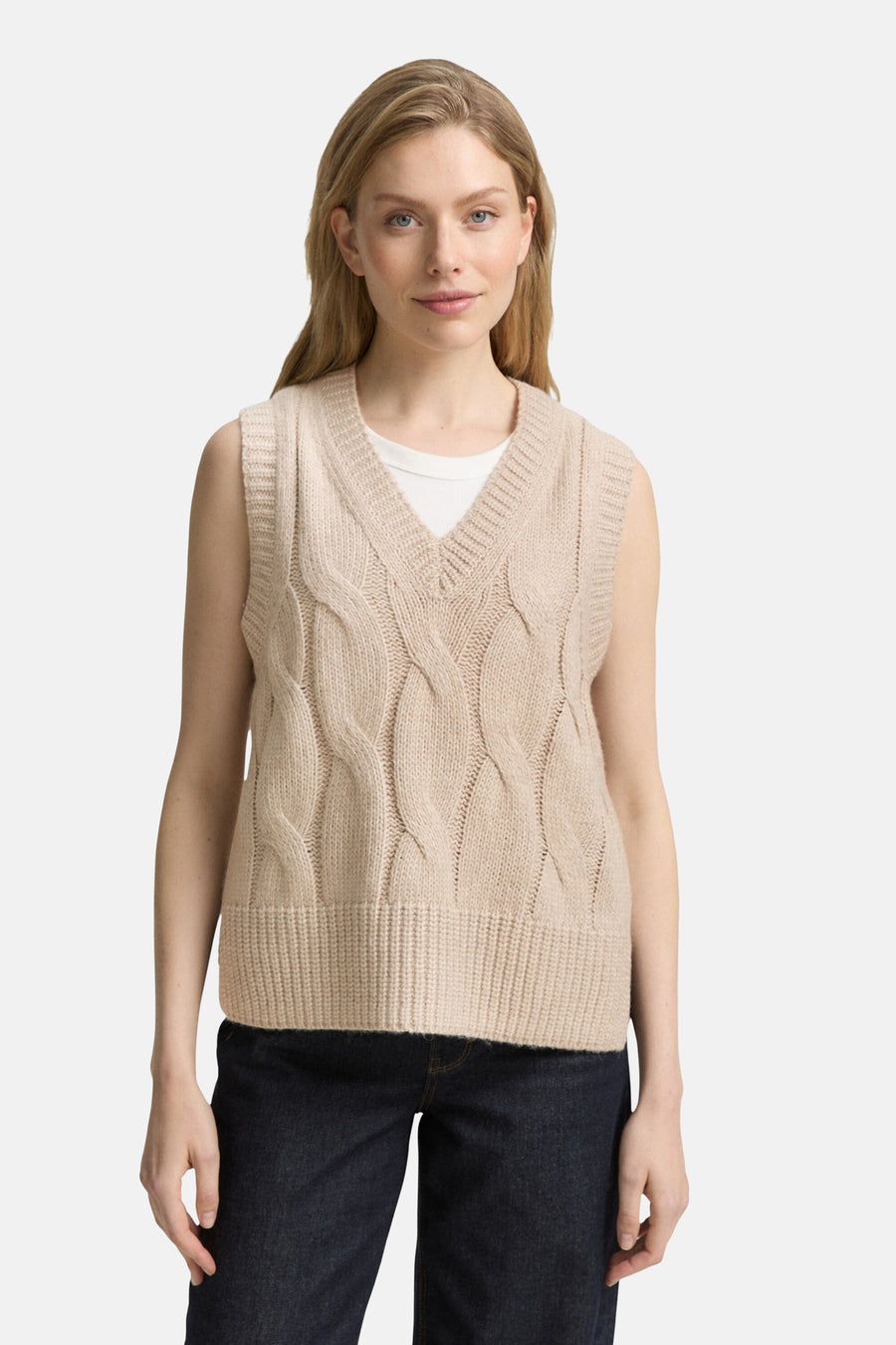 Beige gebreid hemdje van Tom Tailor, met kabelpatroon en geribbelde zoom, gedragen over een wit T-shirt en een donkere jeans.