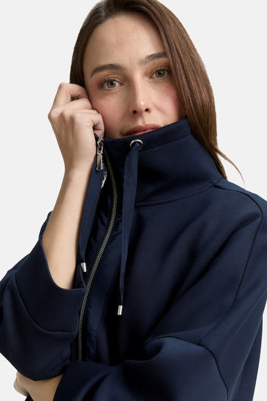 Navy blue zip-front cardigan with high collar and drawstring, cropped front view on model