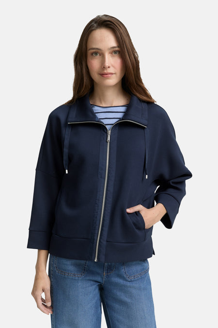 Cardigan bleu en maille de Tom Tailor, avec une fermeture éclair argentée et porté sur un t-shirt rayé.