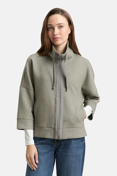 Cardigan kaki de Tom Tailor, avec fermeture éclair et manches trois quarts, porté sur un pull blanc et un jean.
