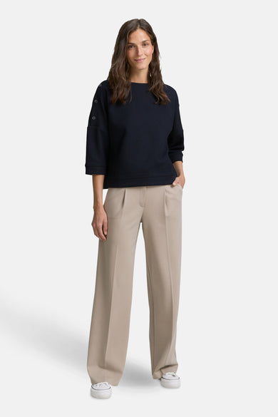 Blauwe sweater van Tom Tailor, driekwart mouwen met knopen, gedragen met een beige broek met hoge taille en witte sneakers.