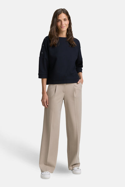 Blauwe sweater van Tom Tailor, driekwart mouwen met knopen, gedragen met een beige broek met hoge taille en witte sneakers.