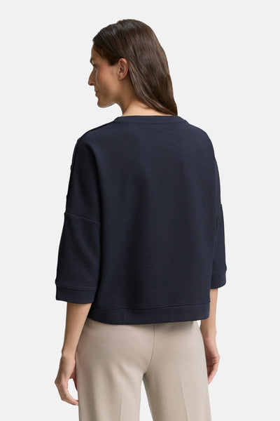 Blauwe sweater van Tom Tailor, met een wafelstructuur en driekwartmouwen, gedragen met een beige broek.