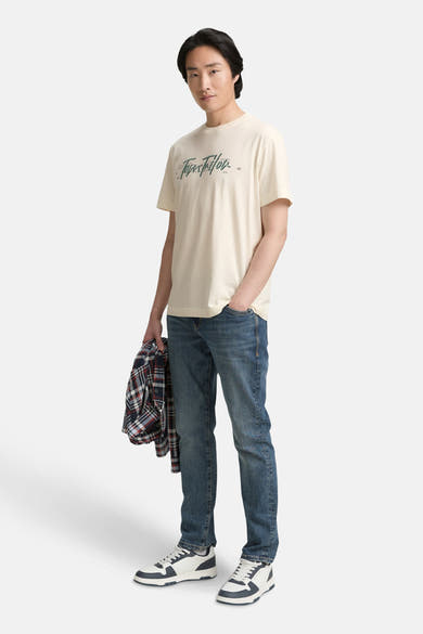 Wit T-shirt met korte mouwen van Tom Tailor, gedragen met een spijkerbroek en sneakers, met een geruit overhemd in de hand.