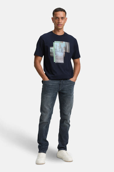 Blauw T-shirt met korte mouwen van Tom Tailor, met een grafische print op de voorkant, gedragen met een spijkerbroek en witte sneakers.