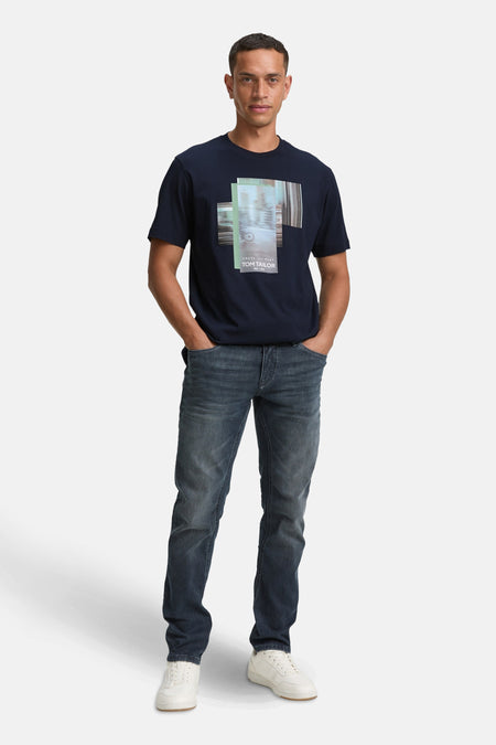 Blauw T-shirt met korte mouwen van Tom Tailor, met een grafische print op de voorkant, gedragen met een spijkerbroek en witte sneakers.