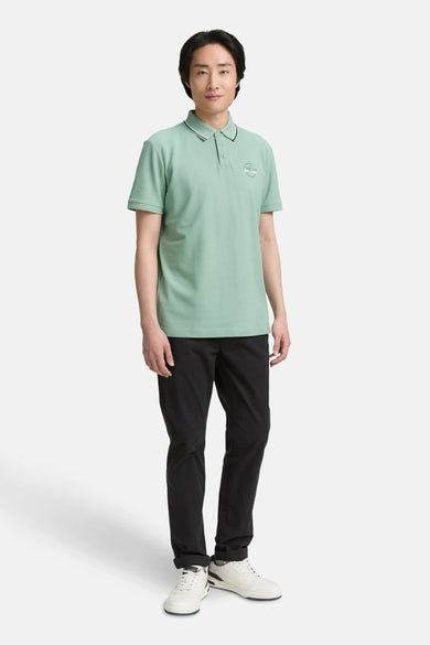 Polo à manches courtes vert de Tom Tailor, avec col et manches soulignés de noir, porté avec un pantalon noir et des baskets blanches.