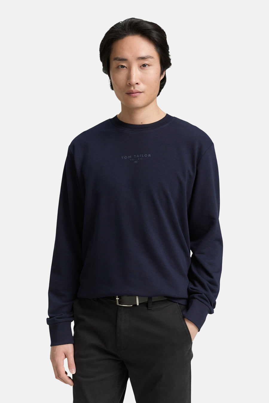 Donkerblauwe rondehals trui van Tom Tailor, met een discreet logo op de voorkant, gedragen met een zwarte broek en een riem.