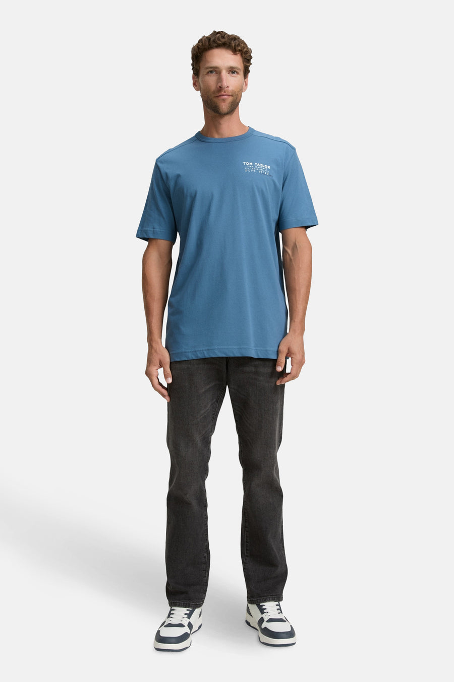 Blauw T-shirt met korte mouwen van Tom Tailor, gedragen met een zwarte jeans en wit-marine sneakers.