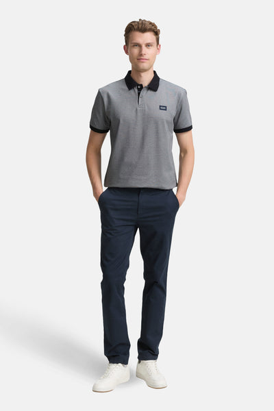 Blauwe gemêleerde polo met korte mouwen van Tom Tailor, met zwarte kraag en mouwboorden, gedragen met een marineblauwe broek en witte sneakers.