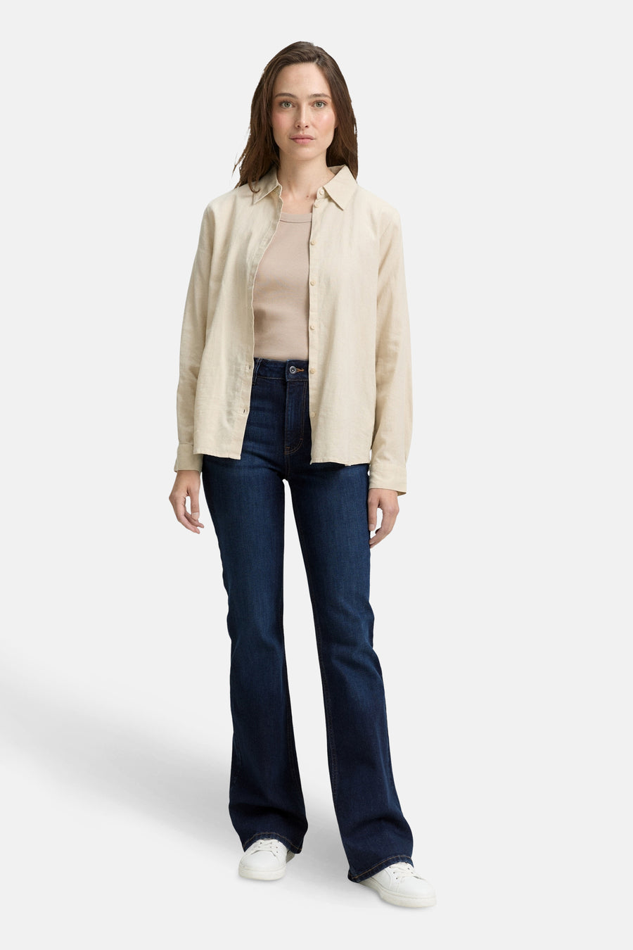 Jean bootcut in donkerblauw denim van Tom Tailor, gedragen met een beige overhemd en witte sneakers.
