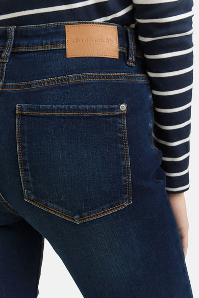 Jean droit en denim bleu foncé par Tom Tailor, avec poche arrière surpiquée et détail boutonné, porté avec un haut rayé.
