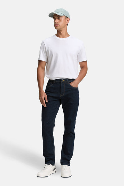 Slim jeans in donkerblauw denim van Tom Tailor, gedragen met een wit T-shirt en witte sneakers.
