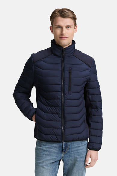 Veste courte bleue par Tom Tailor, matelassée à chevrons avec empiècements texturés aux épaules, portée avec un jean décontracté.