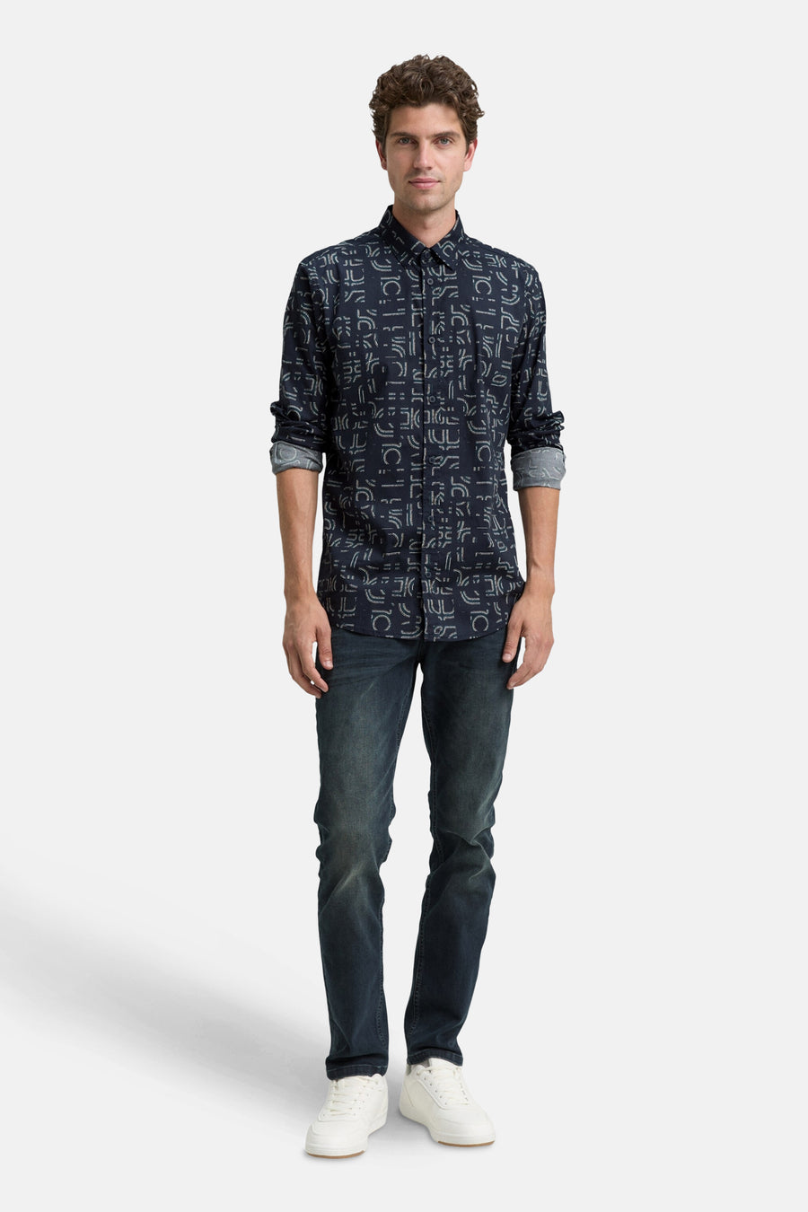 Blauwe blouse met lange mouwen van Tom Tailor, met een geometrisch patroon en gedragen met een spijkerbroek en witte sneakers.
