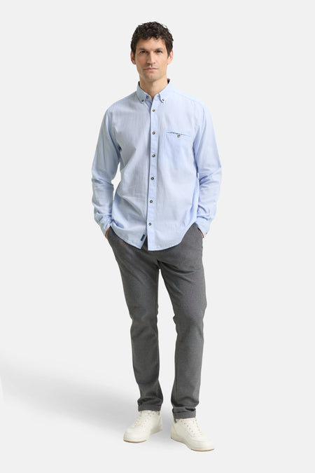Chemise à manches longues bleue de Tom Tailor, portée avec un pantalon gris et des baskets blanches.